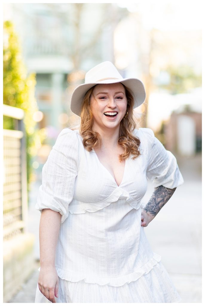 Girl smiling downtown wearing a white dress and hat from boutique