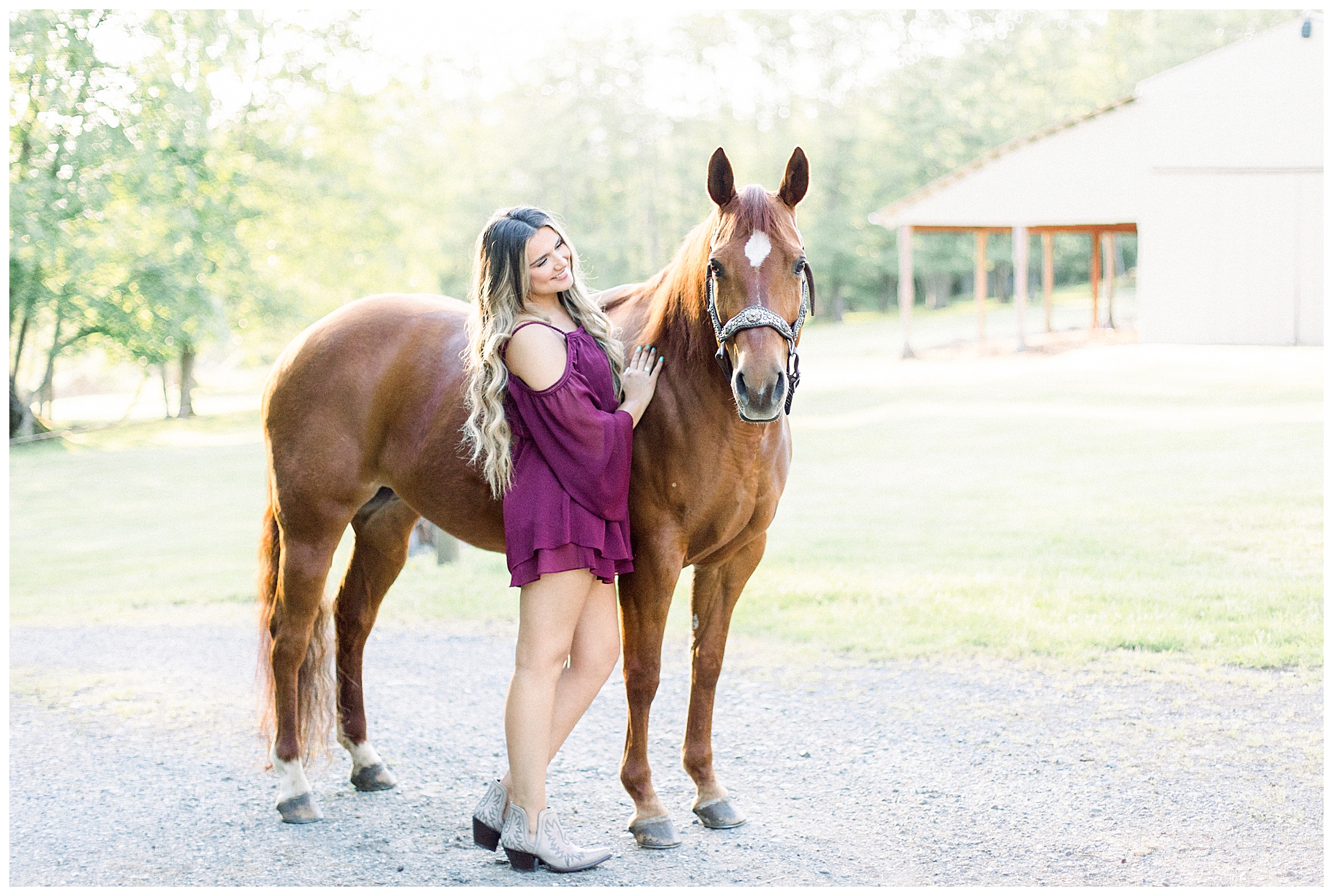 Girl smiling next to her Chestnut horse in front of white barn