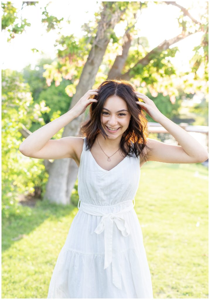 Girl wearing sundress laughs with both hands in her hair