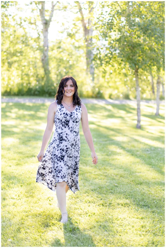 Senior girl walks through grass in dress on sunny evening at River Park in Hamilton, Montana