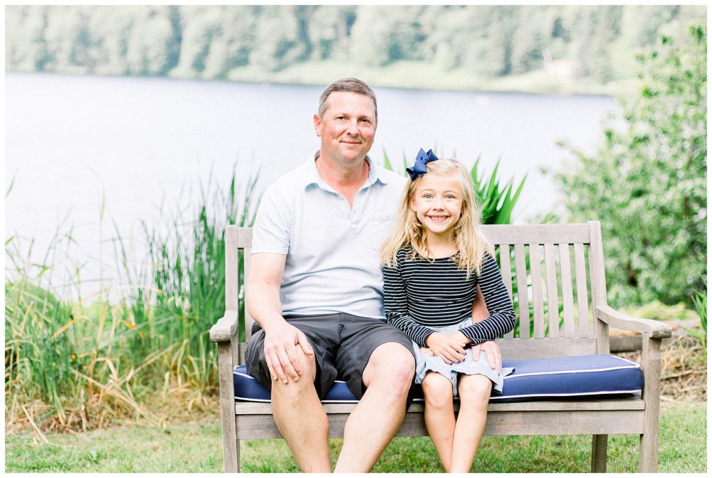 father daughter fall family photos sitting on bench in front of lake wearing pastel blue, navy blue and gray color palette