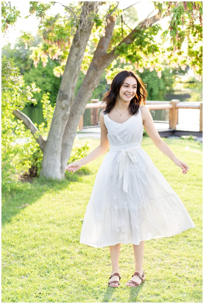 Girl wearing white dress for senior portraits, twirling in park
