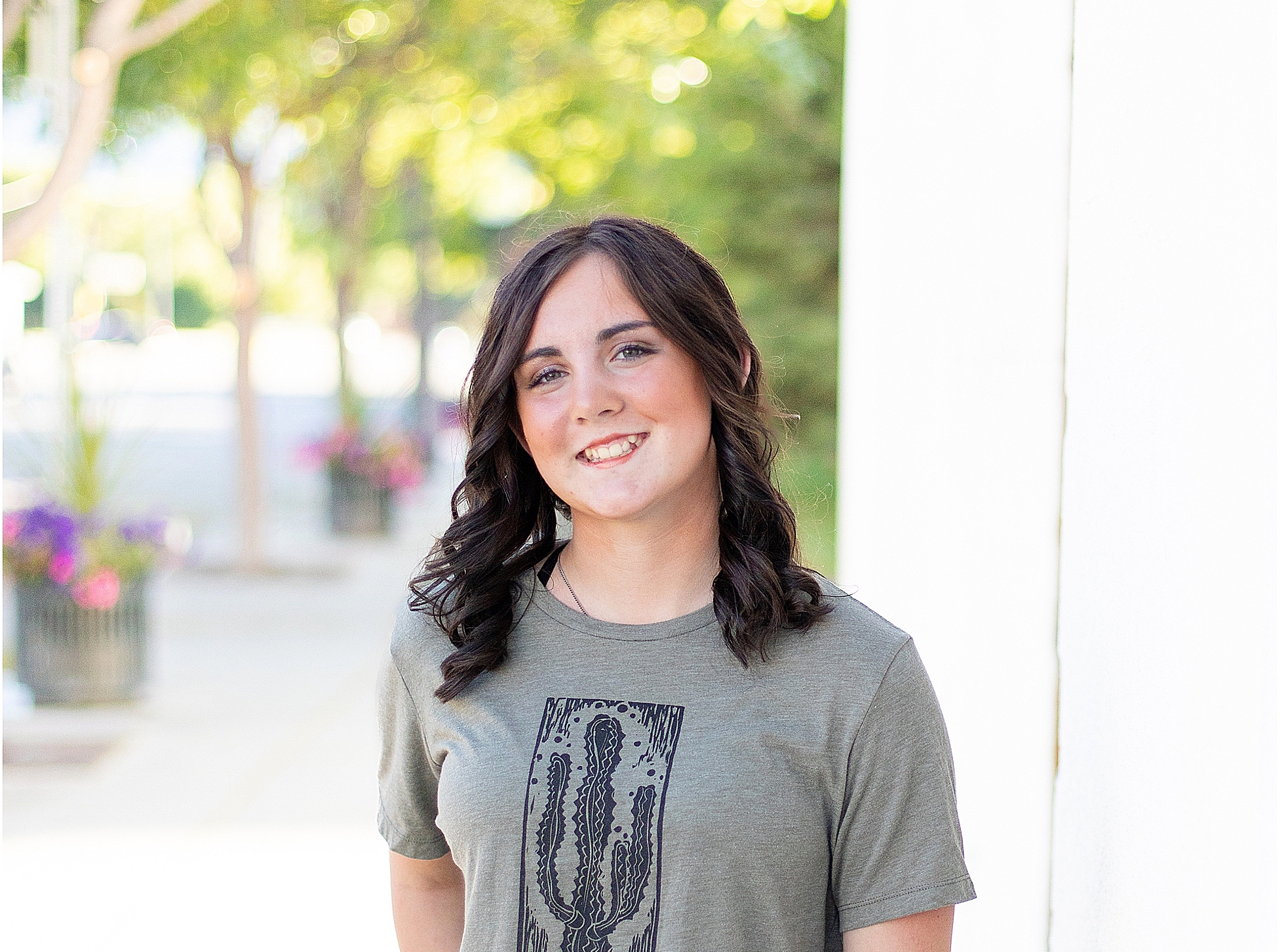 high school senior girl stands in downtown Hamilton, MT smiling wearing a green t-shirt and jeans