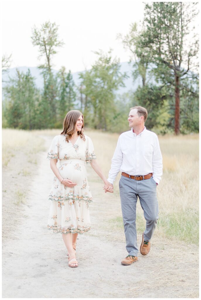 Missoula maternity photos of couple walking down path with mountains in background