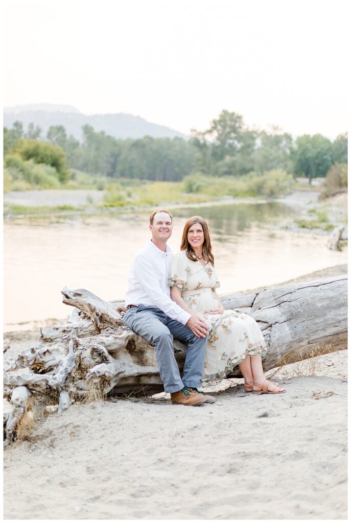 Missoula maternity photos of couple sitting my river on driftwood