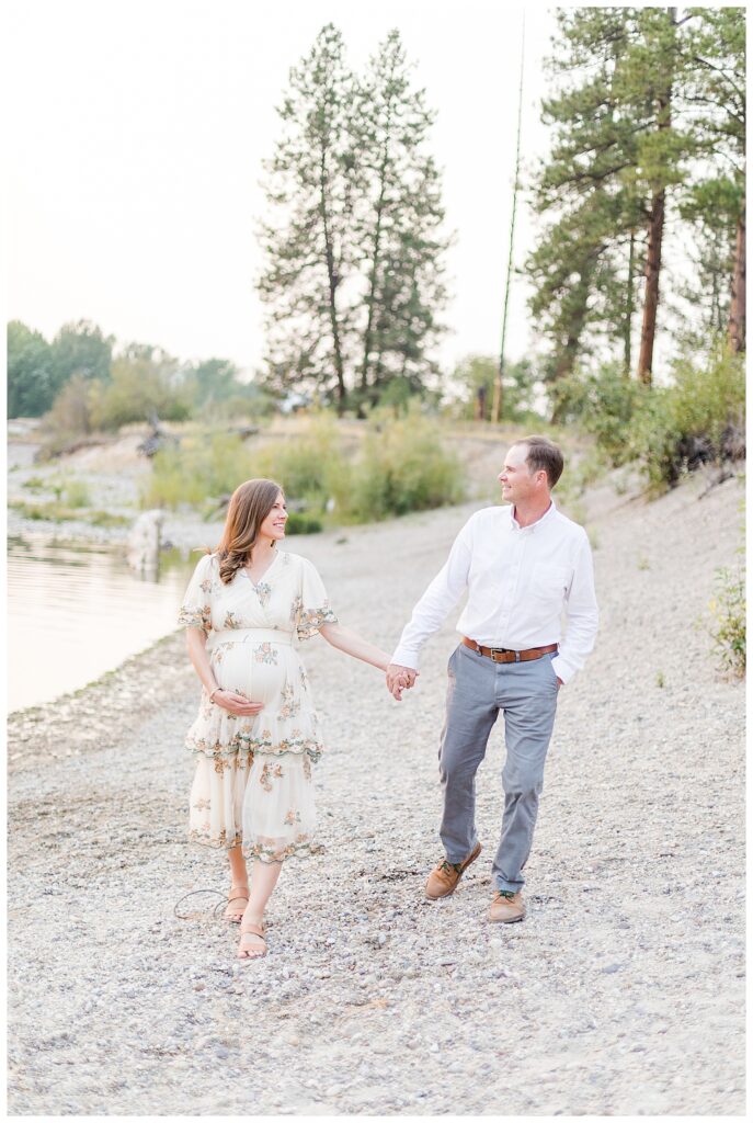 Missoula maternity photos of couple walking on beach of river together smiling