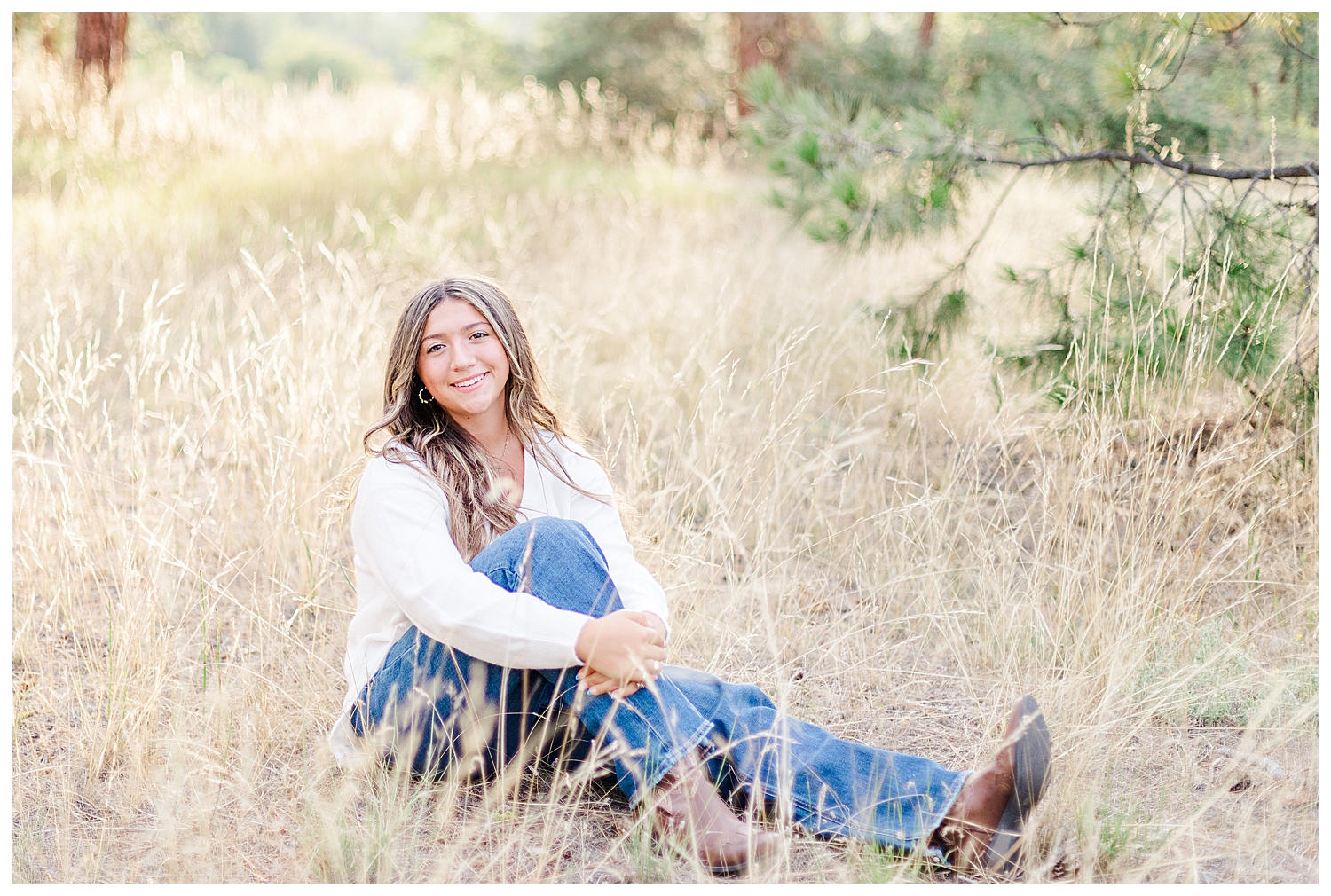 Senior girl sitting in tall grass field smiling at camera for destination Missoula senior photos