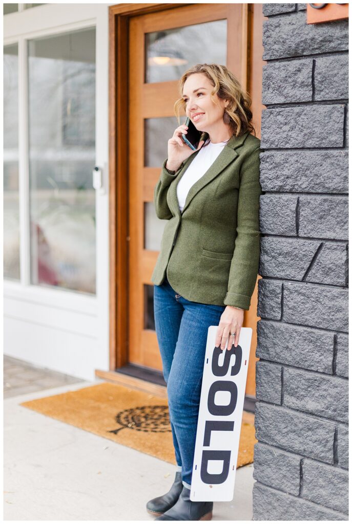 Missoula realtor talking on phone outside of front door holding a sold sign